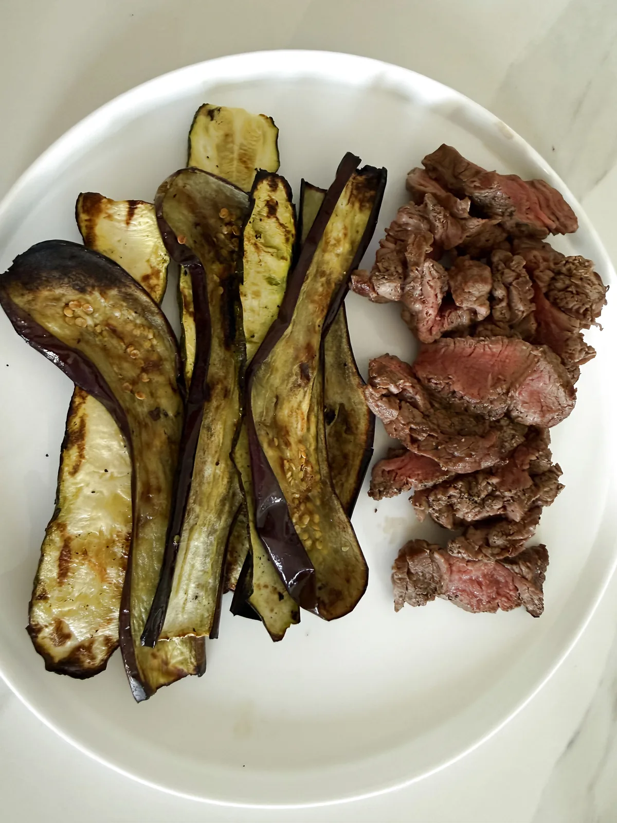 Filet mignon na žaru z mediteranskimi jajčevci na belem krožniku